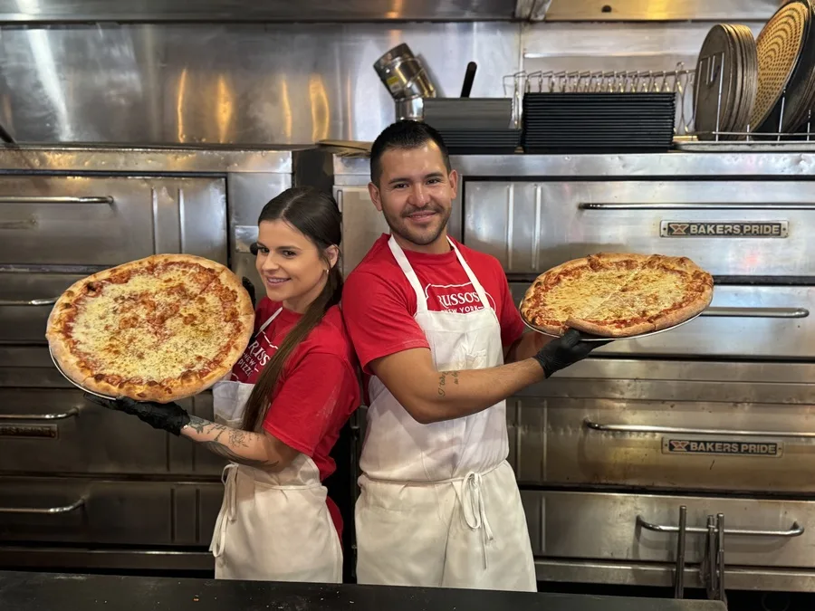 Two Russo's team members presenting freshly baked pizzas
